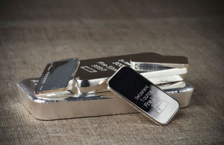 Several silver bars of various weights on a textile texture background.